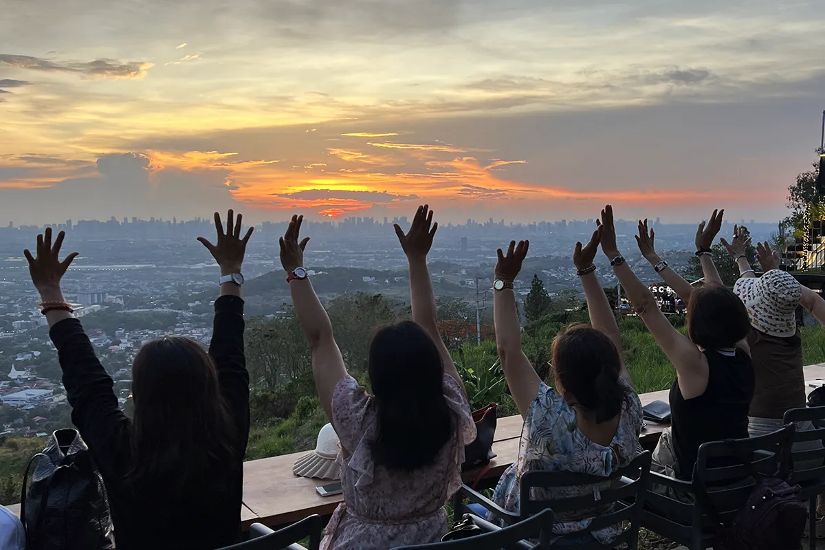 Team members raising hands at a hilltop sunset — Manila